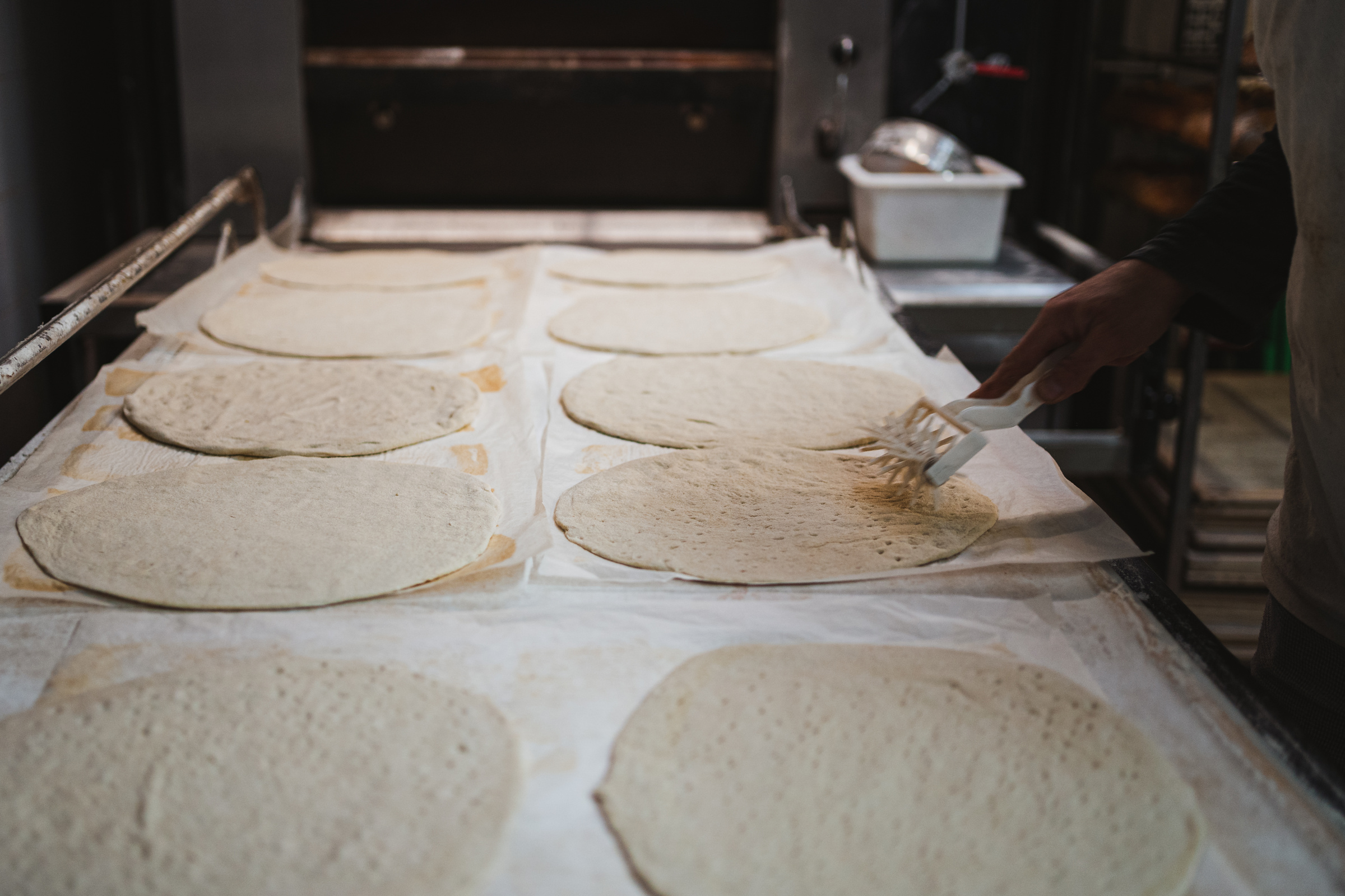 Baker perforating pizza dough base with roller